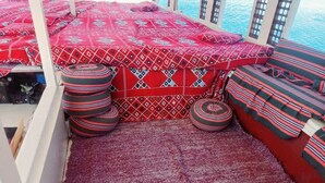 A cozy seating area with patterned cushions and a red carpet, overlooking a body of water.