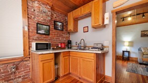 A kitchen with wooden cabinets, a brick wall, a microwave, and a sink.