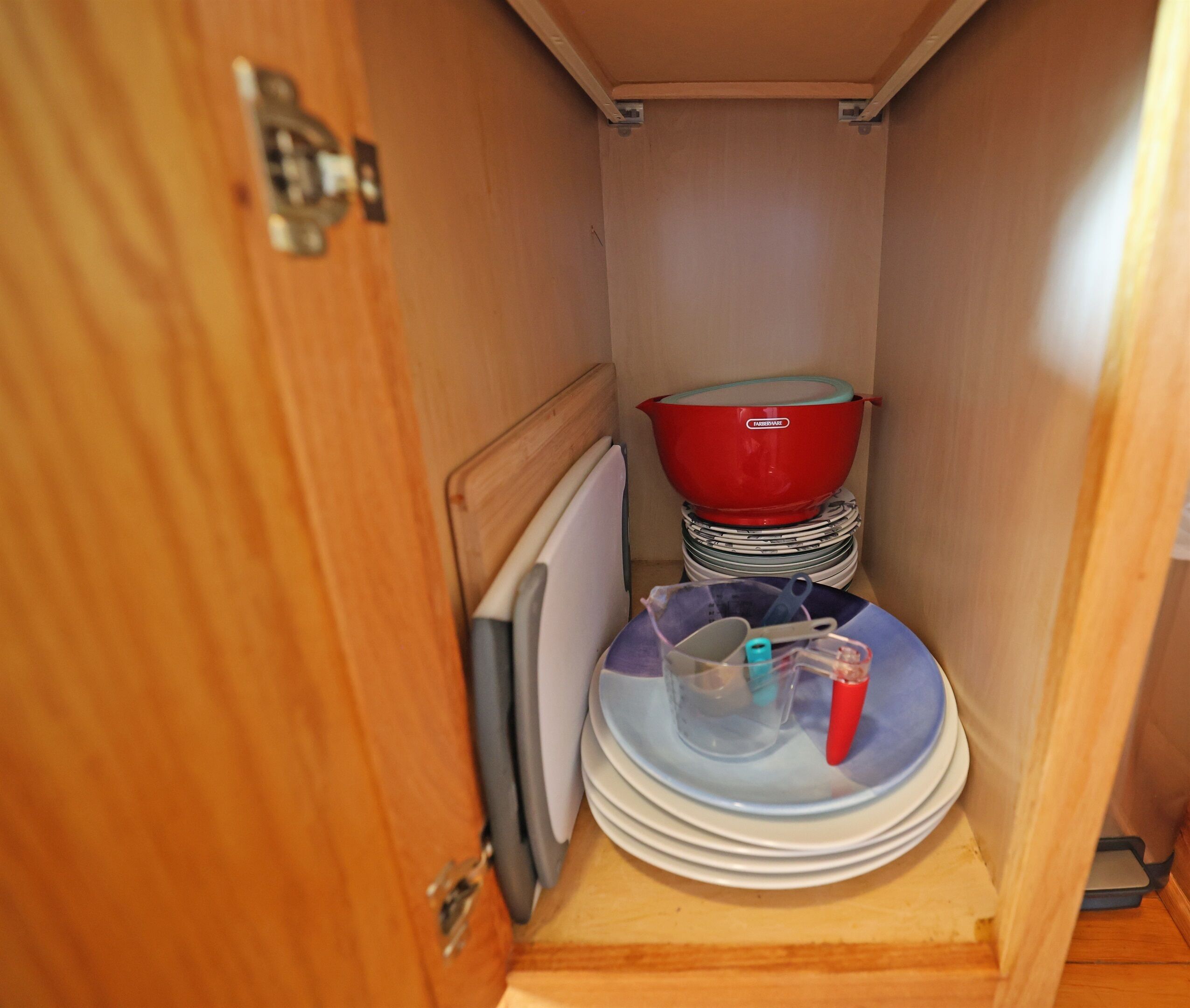 A small kitchen area with a wooden cabinet, a red dish rack, and stacked plates.