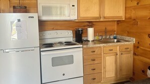A compact kitchen with wooden cabinets, a white refrigerator, a microwave, a stove, and a sink. - Bear Cub ,Cozy cabin with WiFi and AC in peaceful Stevenson (Stevenson)