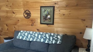 A cozy room with a wooden wall, a framed picture, a grey sofa, and a small table with a lamp. - Bear Cub ,Cozy cabin with WiFi and AC in peaceful Stevenson (Stevenson)