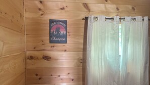 A wooden cabin room with a bed, a nightstand, a power outlet, and a sign on the wall. - Bear Cub ,Cozy cabin with WiFi and AC in peaceful Stevenson (Stevenson)
