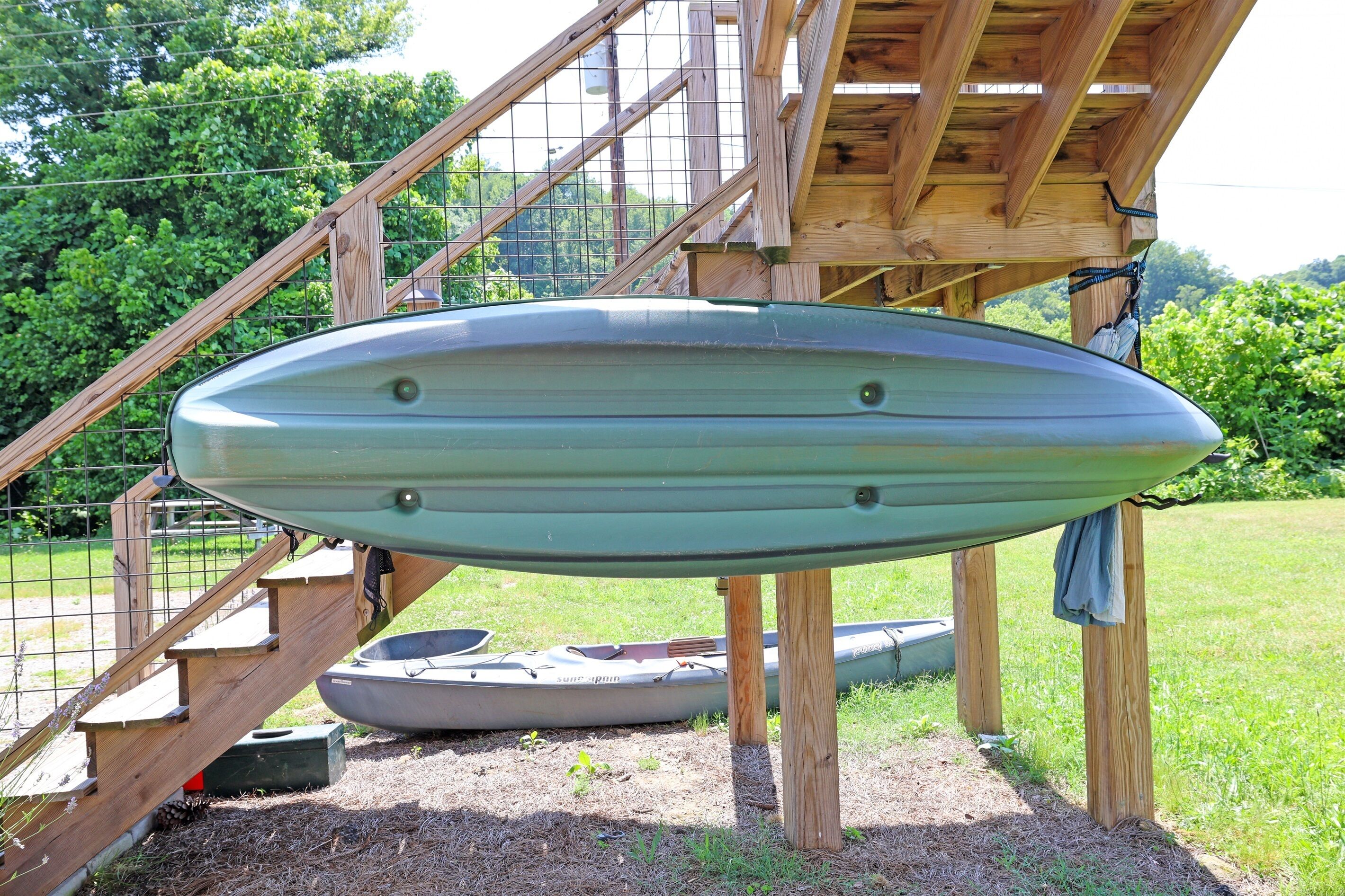 Un kayak bajo una estructura de madera con una cerca de metal y escalones que suben a ella.