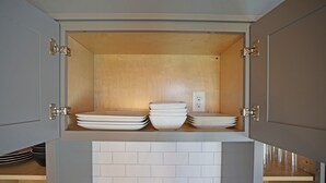 A kitchen cabinet with a wooden interior, a white tiled backsplash, and a power outlet on the wall. - Modern meets Classic: Cozy condo on Smith River (Bassett)