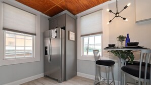 A modern kitchen with a stainless steel refrigerator, two bar stools, a dining table with a blue bottle, and a hanging light fixture. - Modern meets Classic: Cozy condo on Smith River (Bassett)
