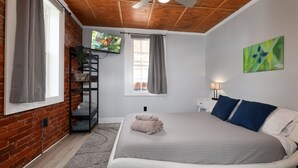 A bedroom with a bed, a TV, a window with curtains, a ceiling fan, and a wall with a painting. - Modern meets Classic: Cozy condo on Smith River (Bassett)