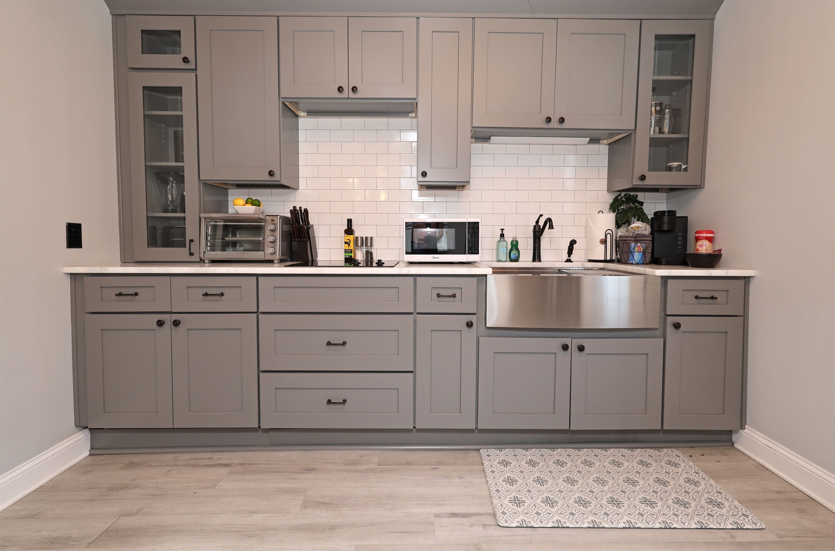 Une cuisine moderne avec des meubles gris, un évier en acier inoxydable et un four à micro-ondes.