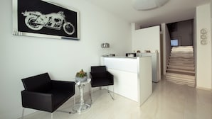 A modern living room with a minimalist design, featuring a black sofa, a small table with a decorative bowl, and a wall-mounted artwork of a motorcycle. - B&B Luna Suite & Room (Rubiera)