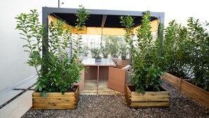 A patio area with a table and chairs under a pergola, surrounded by wooden planters with green plants. - B&B Luna Suite & Room (Rubiera)