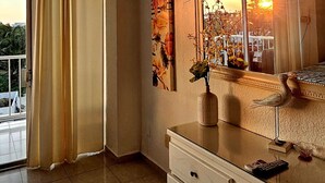Una habitación de hotel con un ventanal grande, un tocador blanco, un espejo y un cuadro en la pared.