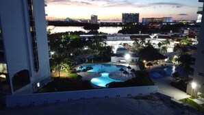 Un hotel con piscina, palmeras y vistas del horizonte urbano al anochecer.