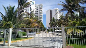 Un área de estacionamiento cerrada con un edificio blanco que lleva la etiqueta "CARISA" al fondo, rodeado de palmeras.
