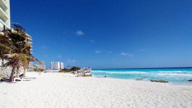 Una playa con arena blanca, palmeras y un cielo azul despejado.