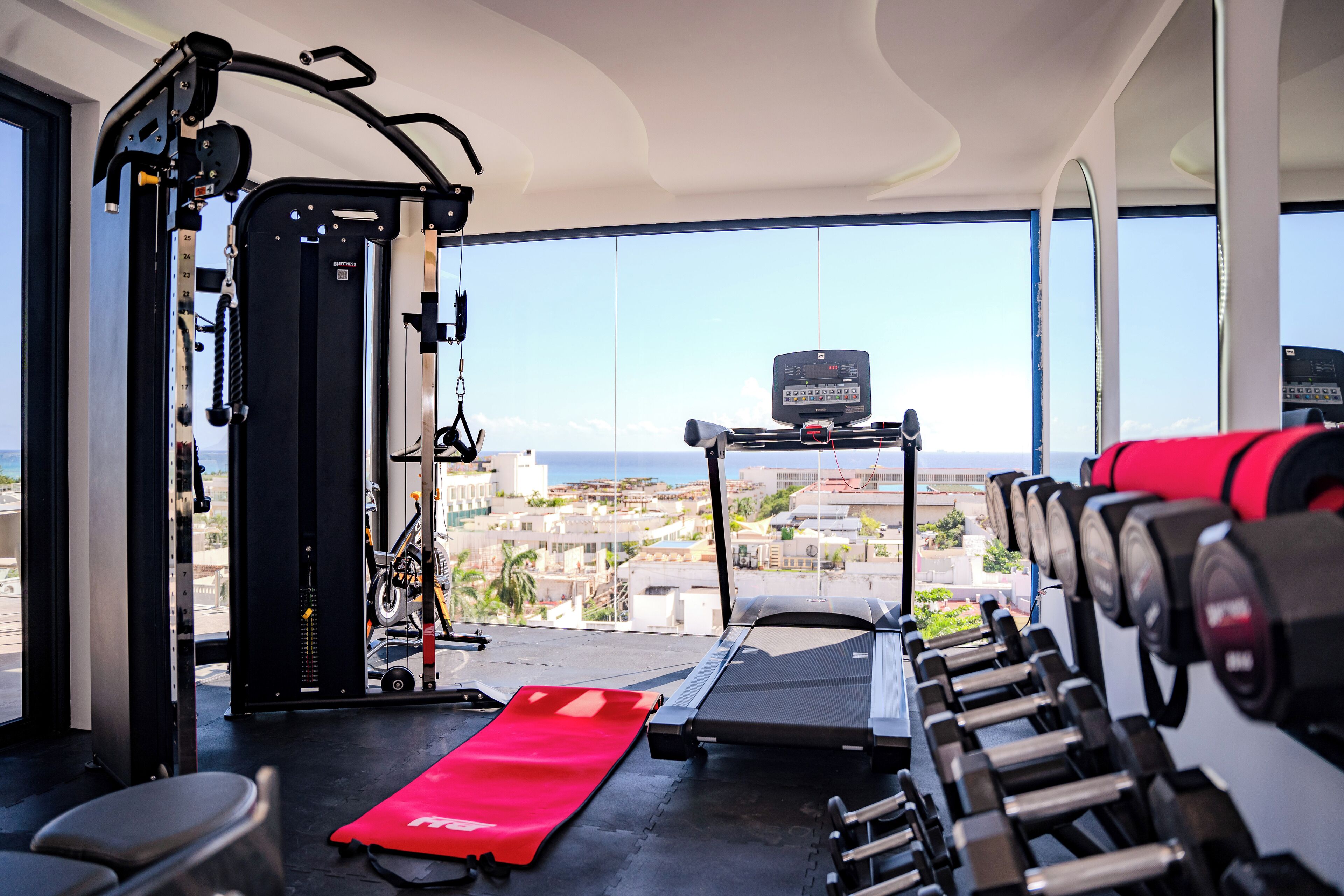 Un gimnasio con cinta de correr, máquinas de pesas y una colchoneta roja.