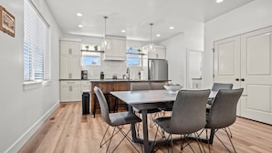 Una cocina moderna con muebles blancos, un refrigerador de acero inoxidable y un comedor con mesa y sillas.