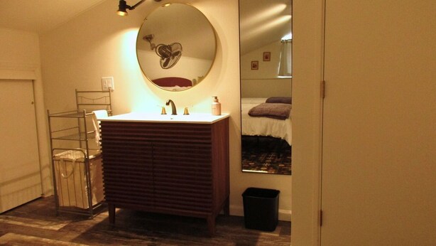 A compact bathroom with a wooden vanity, a round mirror, and a small sink. - The Loft at Aspen Pine with Wi-Fi, AC in wonderful Hot Springs (Hot Springs)