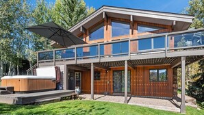 Een modern herenhuis met twee verdiepingen, een glazen balkon, houten gevel en een verzorgd gazon.