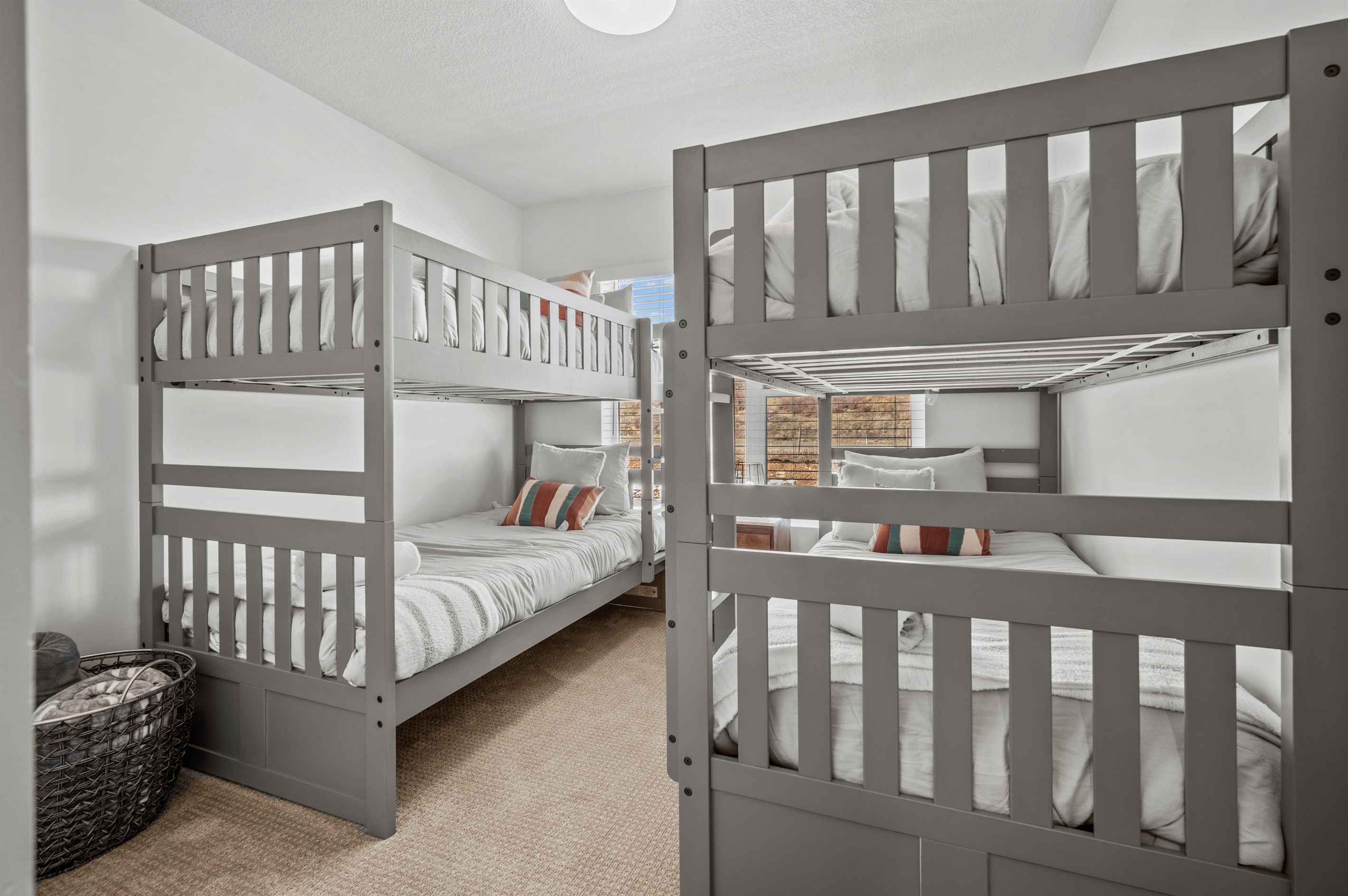 A room with two bunk beds, a small basket, and a window with a view of trees.