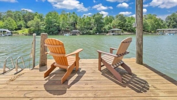 A wooden deck with two Adirondack chairs overlooking a lake, surrounded by trees and a gazebo. - Charming Cottage with Wifi, Screened Porch Just Feet From the Lake (Moneta)