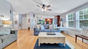 A spacious living room with a ceiling fan, a sofa, a coffee table, and a view of the kitchen in the background. - Charming Cottage with Wifi, Screened Porch Just Feet From the Lake (Moneta)
