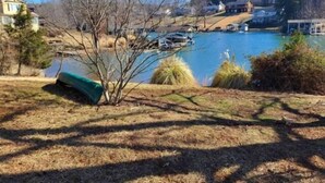 A lake with a dock, a green tarp on the ground, and houses in the background. - Charming Cottage with Wifi, Screened Porch Just Feet From the Lake (Moneta)