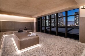 Een moderne hotelkamer met een groot raam en uitzicht over de stad, een ruim interieur en een centraal zithoekje met een kleine tafel en een handdoekhouder.