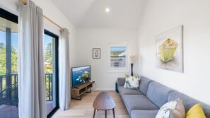 A modern living room with a grey sofa, a television, and a balcony with curtains.