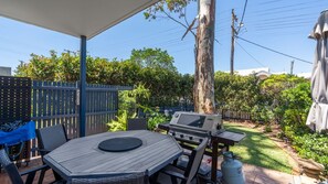 An outdoor patio with a wooden table and chairs, a barbecue grill, and a gas cylinder.