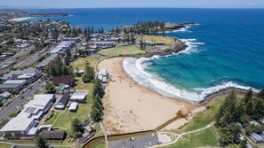 An aerial view of a coastal residential area with a beach, houses, and a parking lot.