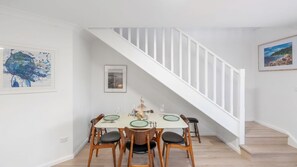 Un coin repas avec un escalier blanc, des chaises en bois et une table dressée pour quatre personnes.