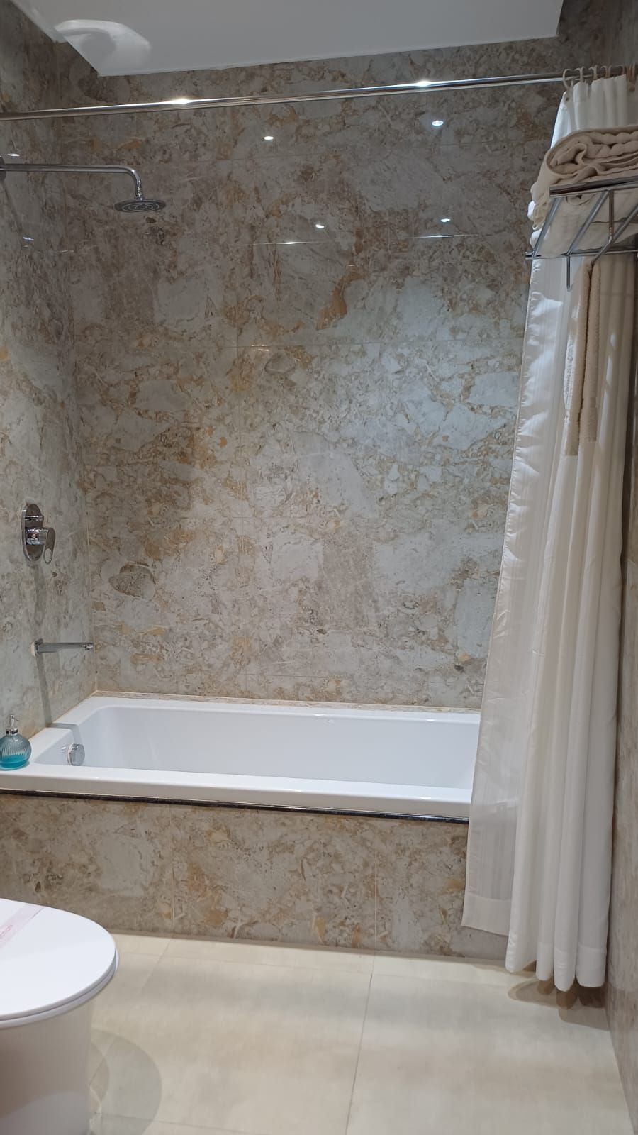 Une salle de bain avec un mur en marbre, une baignoire et un espace douche.