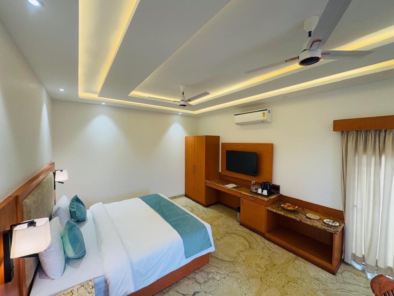 Une chambre d’hôtel équipée d’un lit, d’un bureau, d’une télévision et d’un ventilateur de plafond.