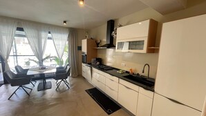 A modern kitchen with white cabinets, a black countertop, and a dining area with a table and chairs. - Luxury Paradise Beach Lagoon (Boa Vista)