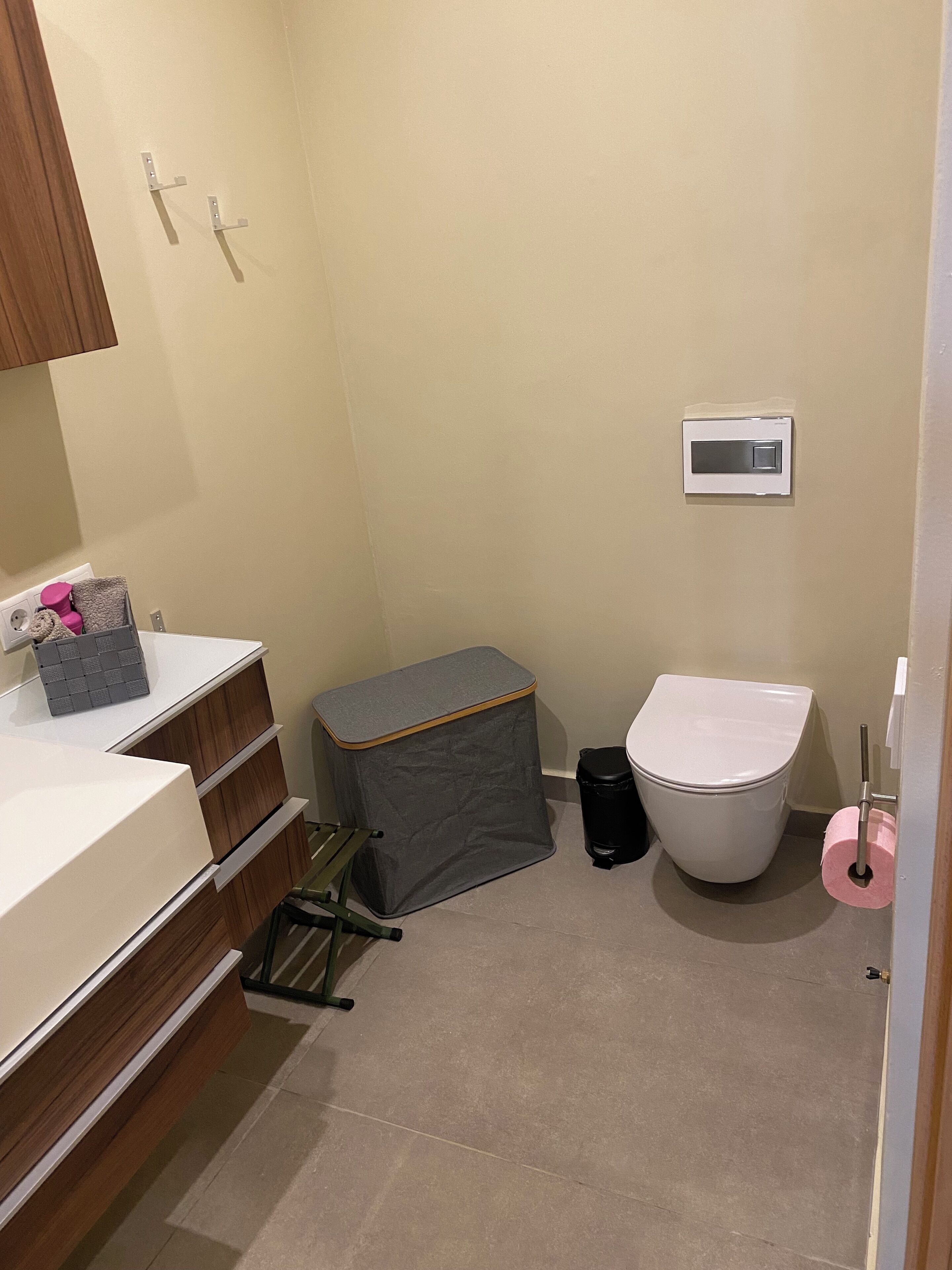 Une petite salle de bain comprenant des toilettes, une poubelle, un petit bac à ordures, un lavabo blanc et un miroir.
