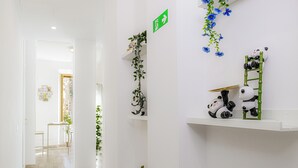 A hallway with white walls, a green emergency exit sign, decorative plants, and shelves with panda figurines. - Green Garden (Rome)