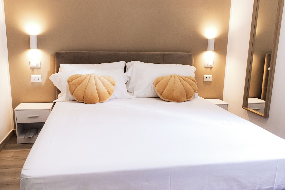 A neatly made bed with white linens and two decorative pillows, flanked by wall-mounted light fixtures.