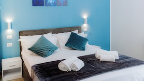 A neatly made bed with white and teal pillows, a dark blanket, and rolled towels on a wooden headboard. - Green Garden (Rome)