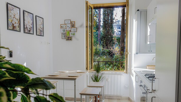 A kitchen with white cabinets, a window with a view of trees, and a potted plant on the windowsill. - Green Garden (Rome)