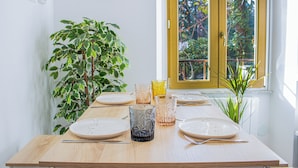 A dining table set with plates, cutlery, and glassware, with a potted plant and a window with a view of greenery. - Green Garden (Rome)