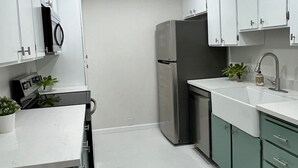 Una cocina moderna con armarios blancos, un refrigerador de acero inoxidable, un lavamanos y una encimera con una planta.