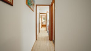 Un pasillo estrecho con piso de madera que conduce a un baño con inodoro y lavabo.