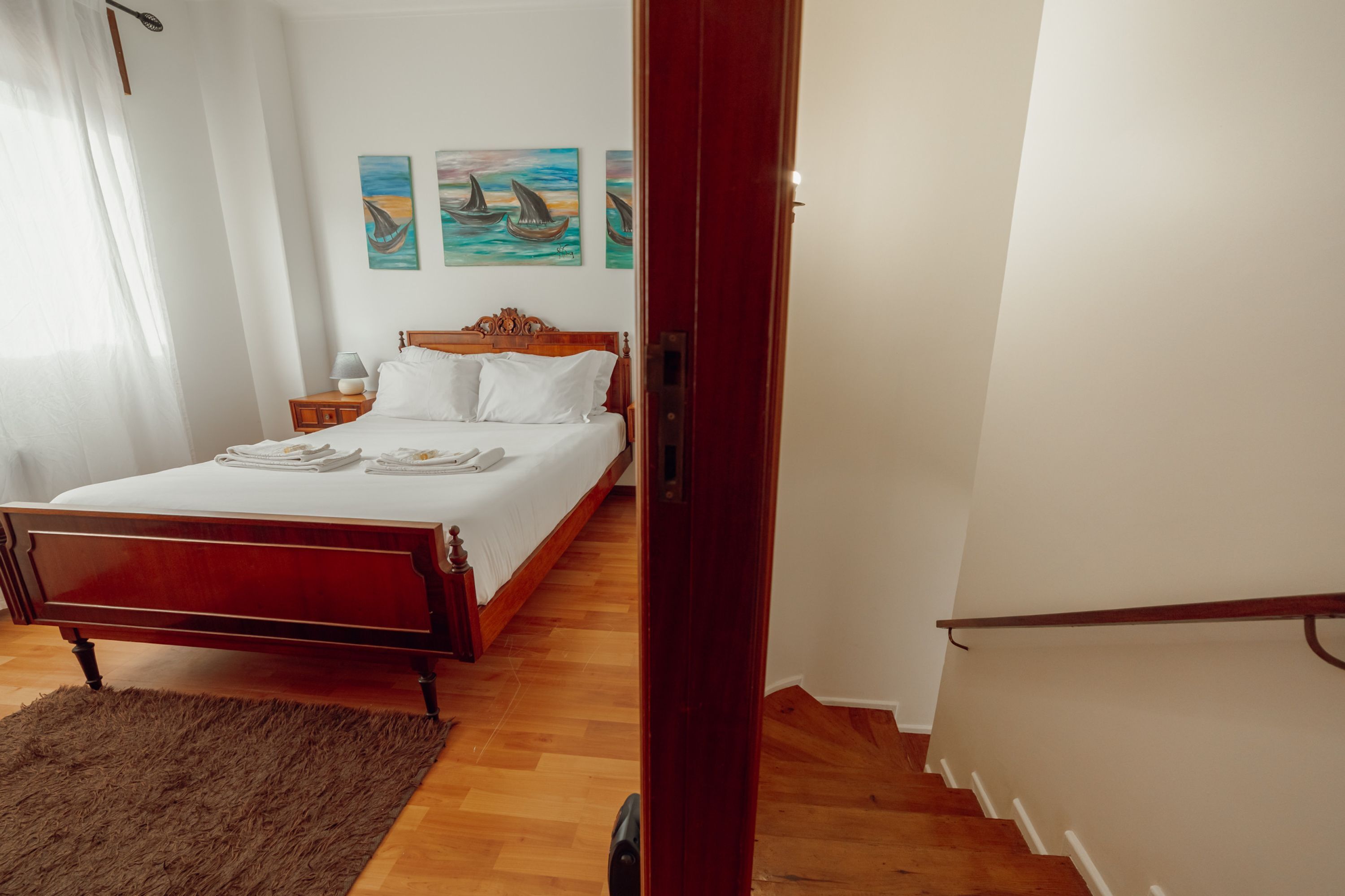 A bedroom with a wooden bed, white linens, a fluffy rug, and two paintings on the wall.