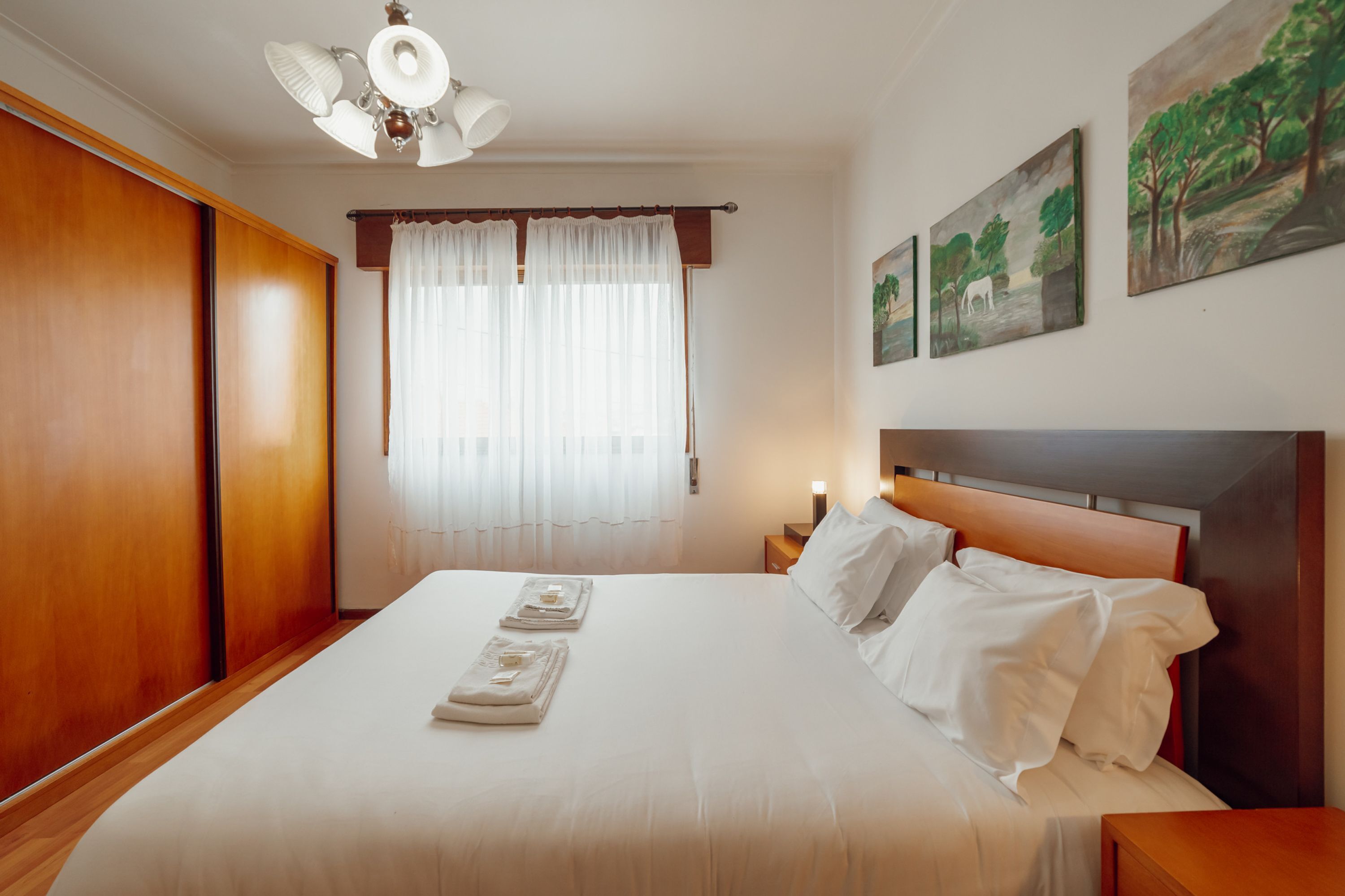 A neatly made bed with white linens and towels, a wooden headboard, and a nightstand with a lamp.