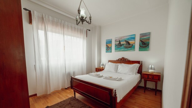 Un dormitorio con una cama de madera, ropa de cama blanca, una alfombra mullida y una obra de arte en la pared.