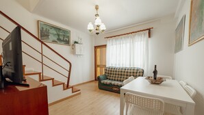 Una sala de estar con una escalera, un sofá, una mesa de comedor y un televisor.