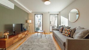 A modern living room with a grey sofa, a wooden TV stand, a round mirror, and a small round table. - Gaia Premium B Apartment by Vacationy (Vila Nova de Gaia)