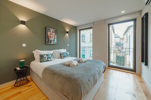 A modern bedroom with a large bed, a small side table, a wall-mounted light, and a window with a view of buildings. - Gaia Premium B Apartment by Vacationy (Vila Nova de Gaia)