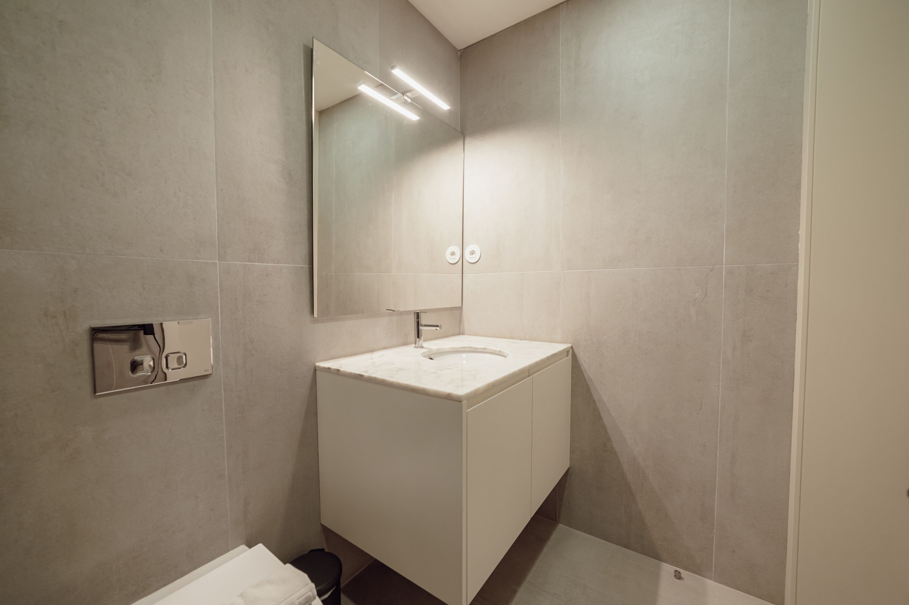 A modern bathroom with a white vanity, a large mirror, and a wall-mounted light fixture.
