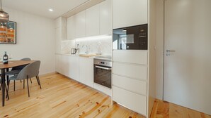 A modern kitchen with white cabinets, a built-in oven, and a dining area with a table and chairs. - Gaia Premium B Apartment by Vacationy (Vila Nova de Gaia)