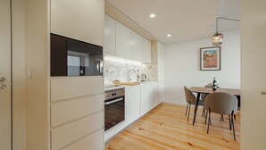 Una cocina moderna con armarios blancos, horno empotrado y comedor con mesa y sillas de madera.